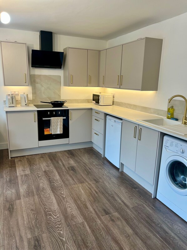 A modern kitchen with a built-in oven, microwave, and dishwasher, and a washing machine in the corner. - Luxury Apartment Smart tv - Sofa bed (Huddersfield)