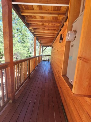 A wooden deck with a railing, leading to a covered area with a ceiling and a wall-mounted heater. - New built log home designed with elegance, charm and finish with 360 vi (Arnold)