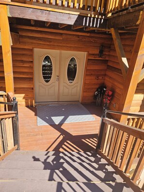 Uma cabana de madeira com porta dupla, escada de madeira e corrimão de metal.