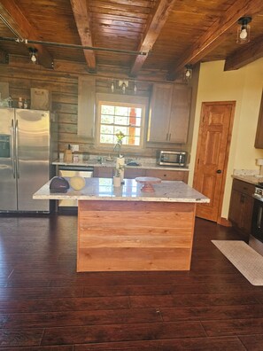 A kitchen with wooden cabinets, a stainless steel refrigerator, a microwave, and a wooden island with a sink. - New built log home designed with elegance, charm and finish with 360 vi (Arnold)
