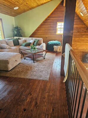 Uma sala de estar estilo loft com teto de madeira, um conjunto de sofás, uma mesa de centro e vista para o exterior.