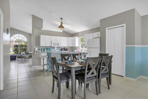 Cozinha moderna com armários brancos, área de jantar com mesa e cadeiras, e uma janela grande.