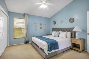 Quarto com cama, mesa de cabeceira, ventoinha no teto e decorações nas paredes.