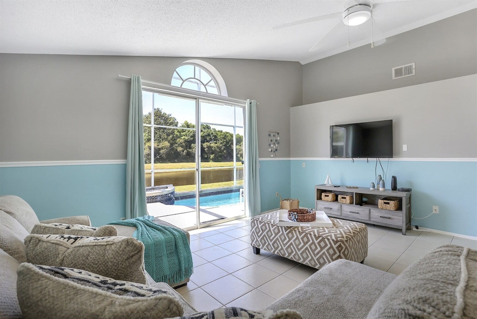 Una sala de estar con vista a la piscina, un televisor y una decoración en tonos grises y azules.