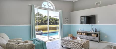 Una sala de estar con vista a la piscina, un televisor y una decoración en tonos grises y azules.