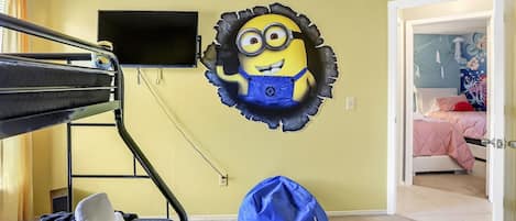 A bunk bed with a TV mounted above it, a blue bean bag chair, and a Minion wall decal in a room with yellow walls.