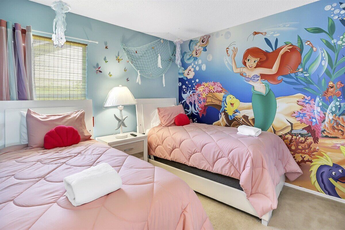 Een slaapkamer met twee bedden, een muurschildering van een zeemeermin en een zeester decoratie aan de muur.