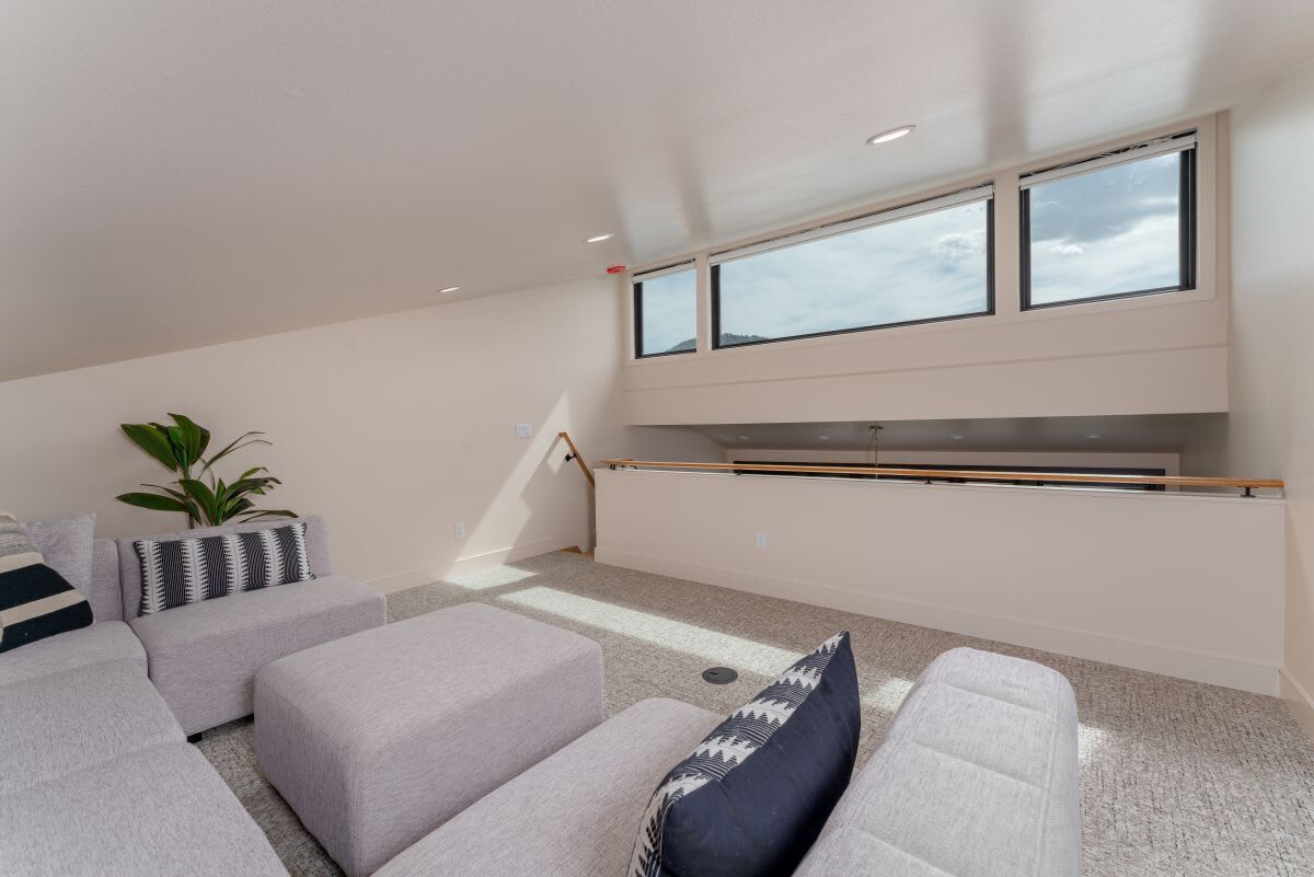 A modern living room with a sofa set, a coffee table, and a plant. There are large windows providing natural light.