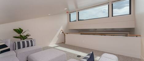 A modern living room with a sofa set, a coffee table, and a plant. There are large windows providing natural light.
