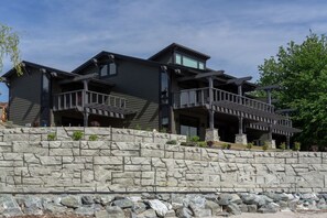 A modern two-story house with a stone retaining wall, multiple balconies, and a covered outdoor area. - Lakefront Condo B4  Pool in Wapato Point Chelan (Manson)
