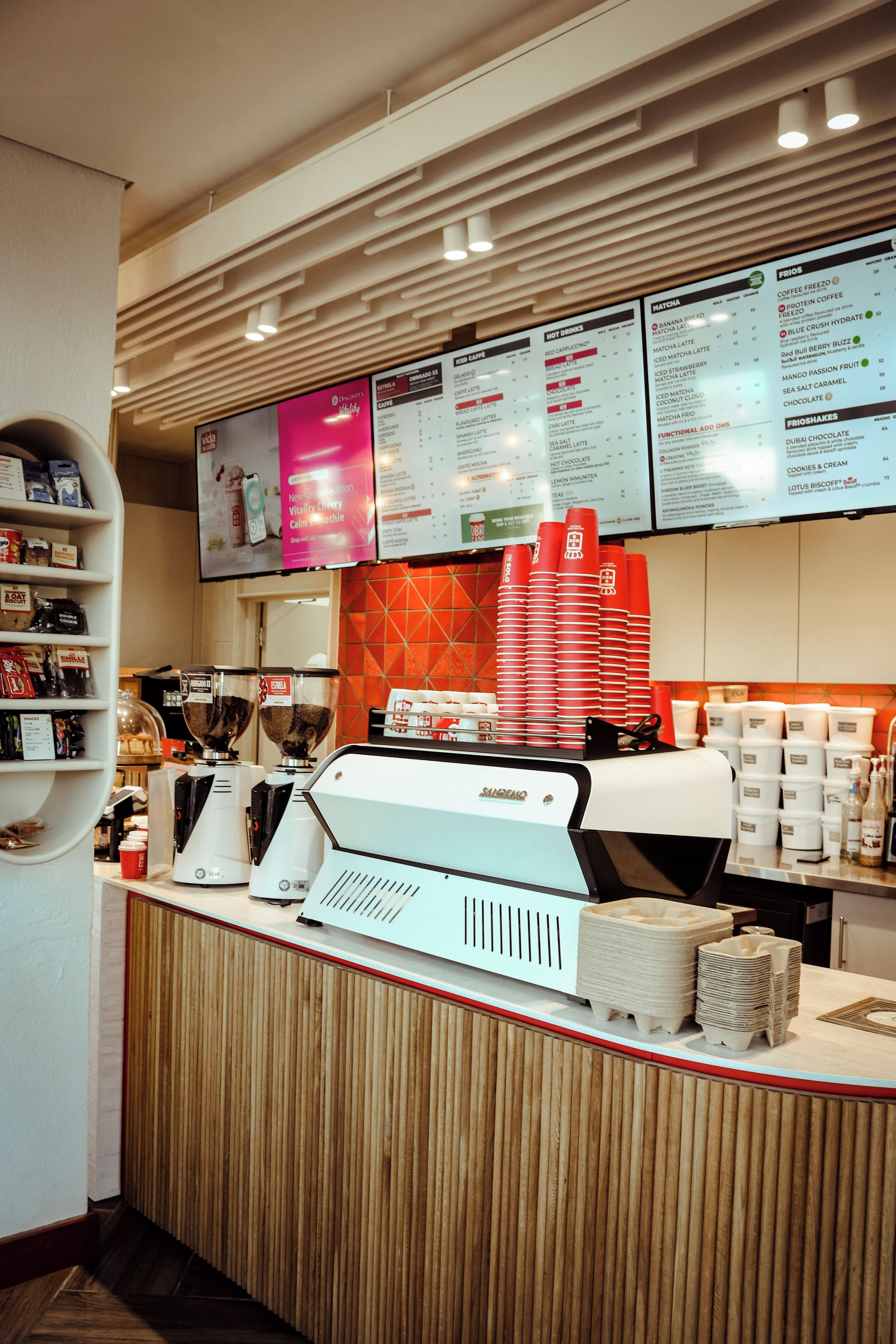 Een café toonbank met een menubord erboven, een koffieapparaat en stapels wegwerpbekers.