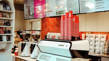 Een café toonbank met een menubord erboven, een koffieapparaat en stapels wegwerpbekers.