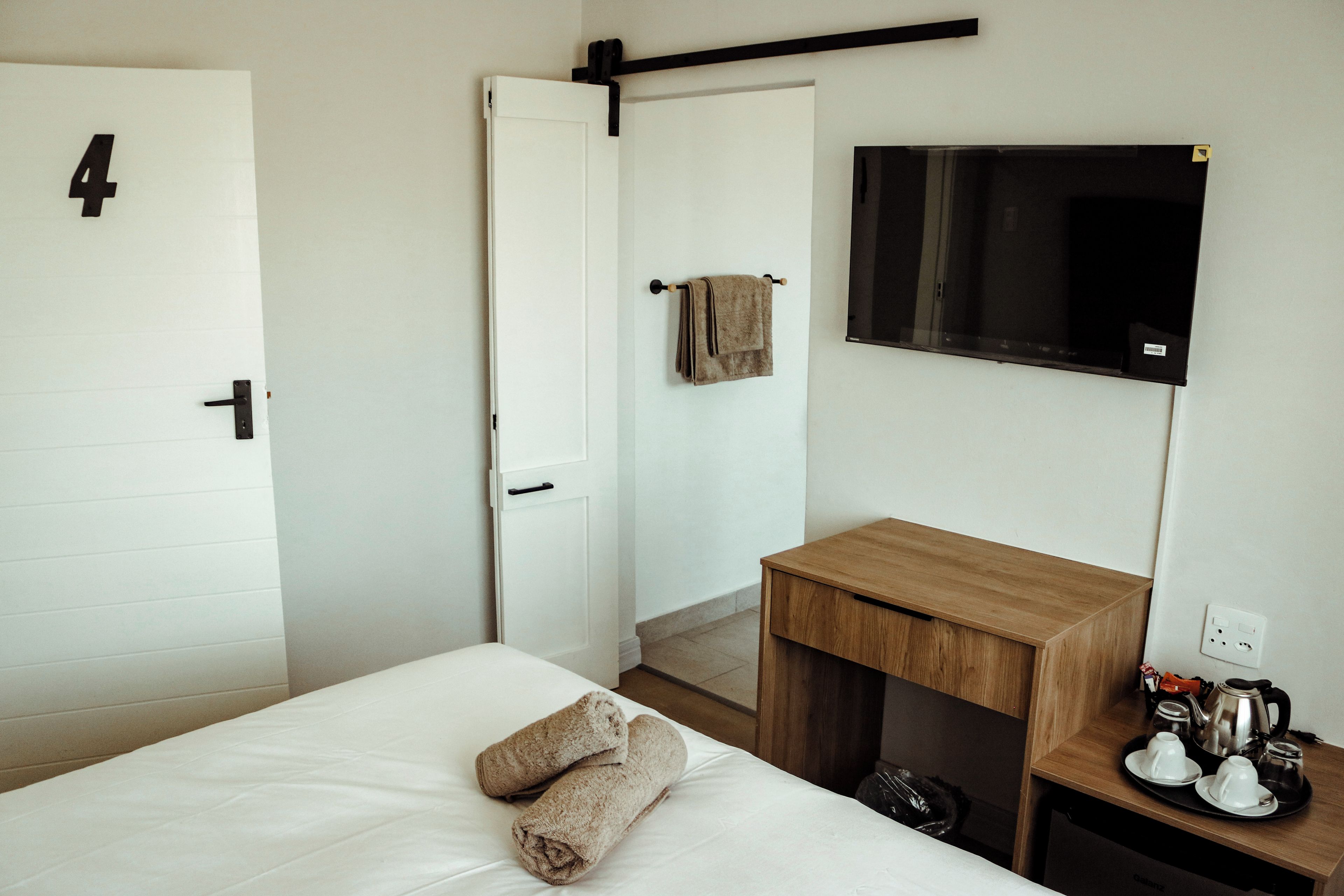 Una camera d'albergo con un letto, un comodino in legno, una TV a parete e una porta con il numero 4.