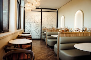 Interior de restaurante con mesas redondas, asientos acolchados y un separador con diseño geométrico.