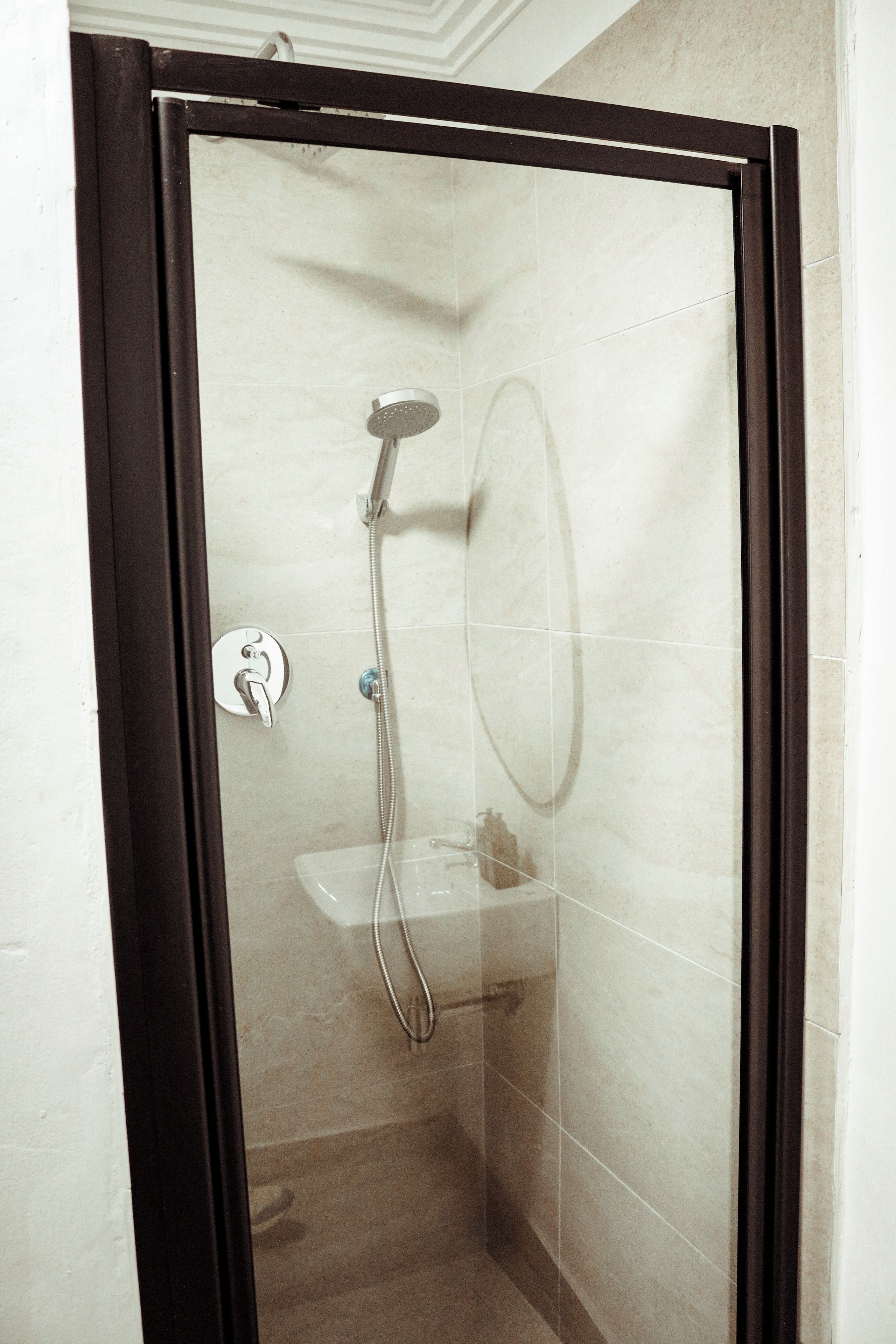 Un espace douche clos par des parois en verre, doté d’un pommeau de douche à main, d’un robinet mural et d’un petit lavabo avec un miroir.