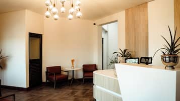 A reception area with a wooden reception desk, two brown leather chairs, a small table with a vase, and a hanging light fixture.