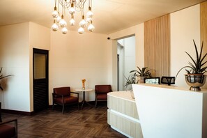 Un área de recepción con un mostrador de madera, dos sillones de cuero marrón, una mesita con un jarrón y una lámpara colgante.
