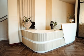 Un mostrador de recepción con listones verticales de madera, dos plantas en macetas y una silla moderna.