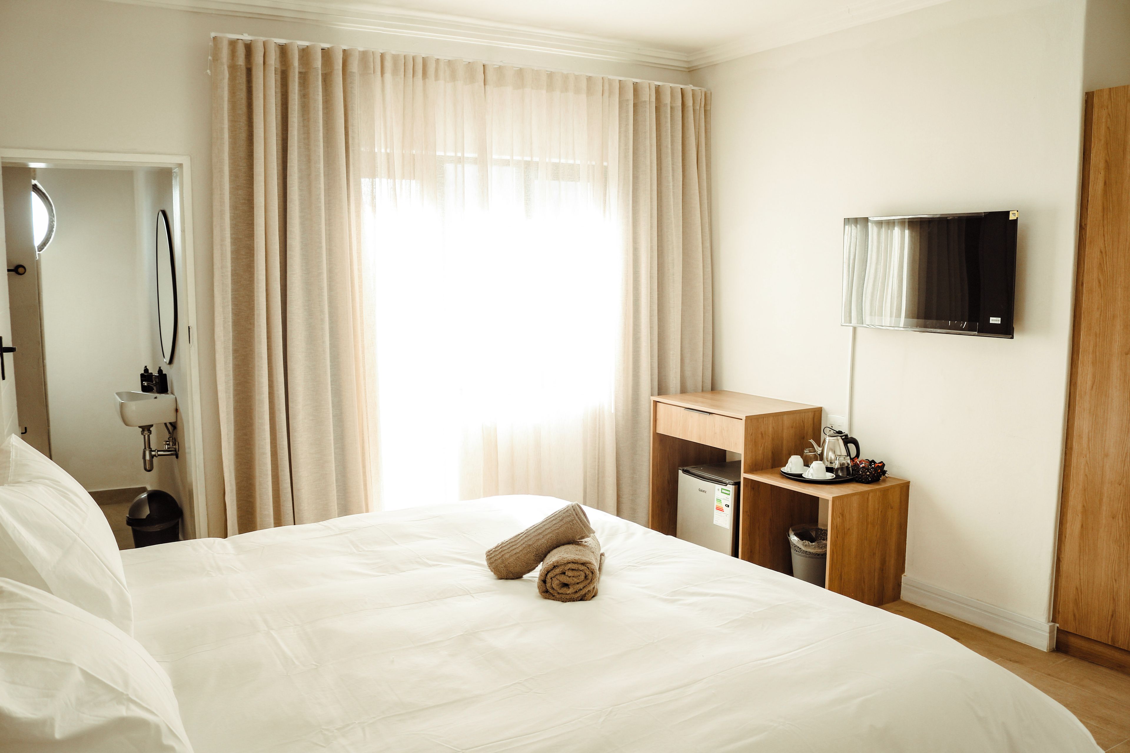 Een hotelkamer met een groot bed, een houten nachtkastje, een aan de muur bevestigde televisie en een raam met gordijnen.