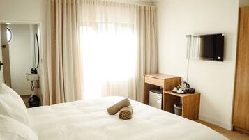 Een hotelkamer met een groot bed, een houten nachtkastje, een aan de muur bevestigde televisie en een raam met gordijnen.