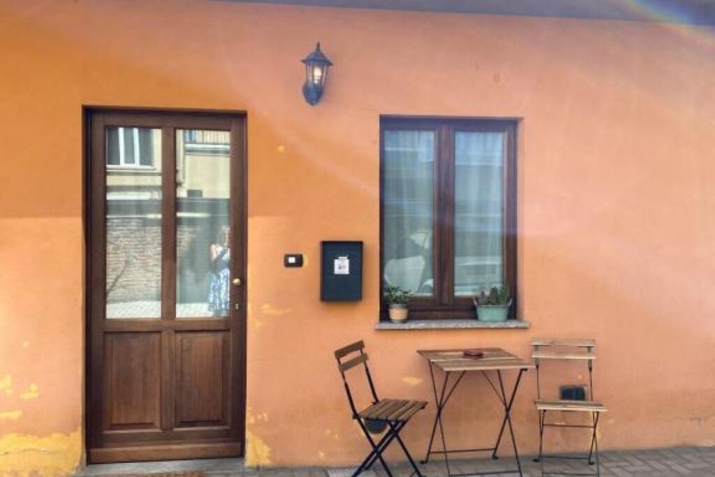 Ein Gebäude mit einer Holztür, einem fenster mit Vorhängen und einem kleinen Tisch mit Stühlen davor.