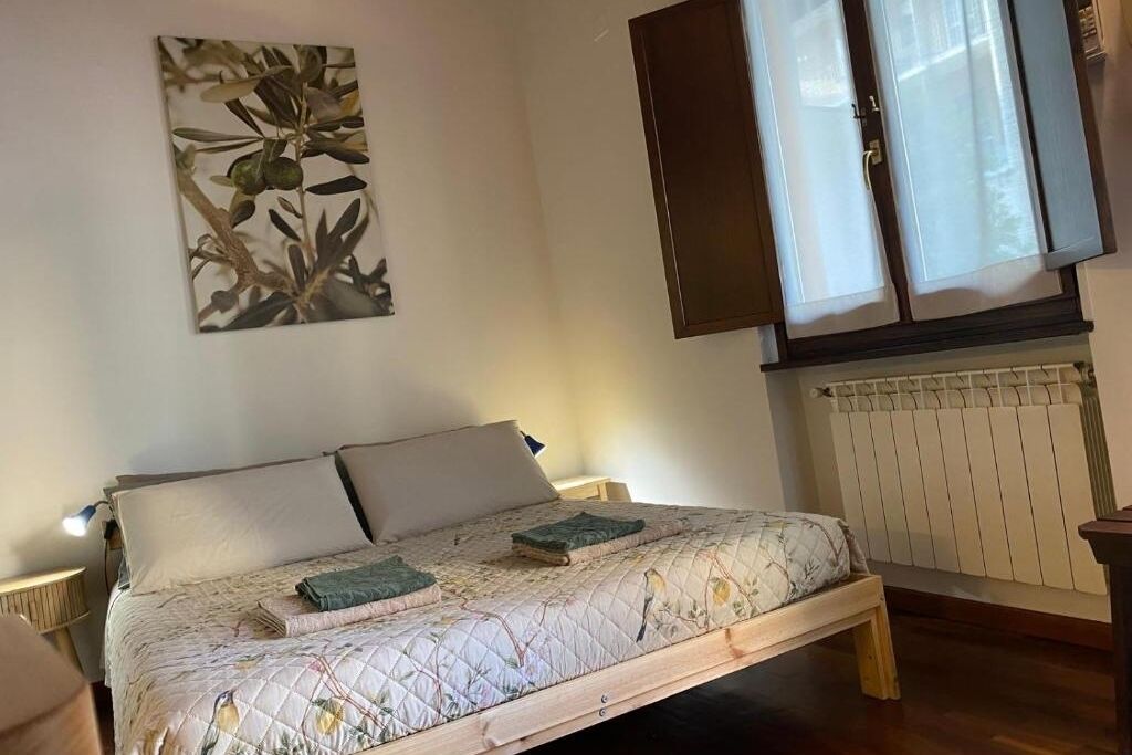 Une chambre à coucher avec un lit, une fenêtre avec des rideaux, un radiateur et une œuvre d’art accrochée au mur.