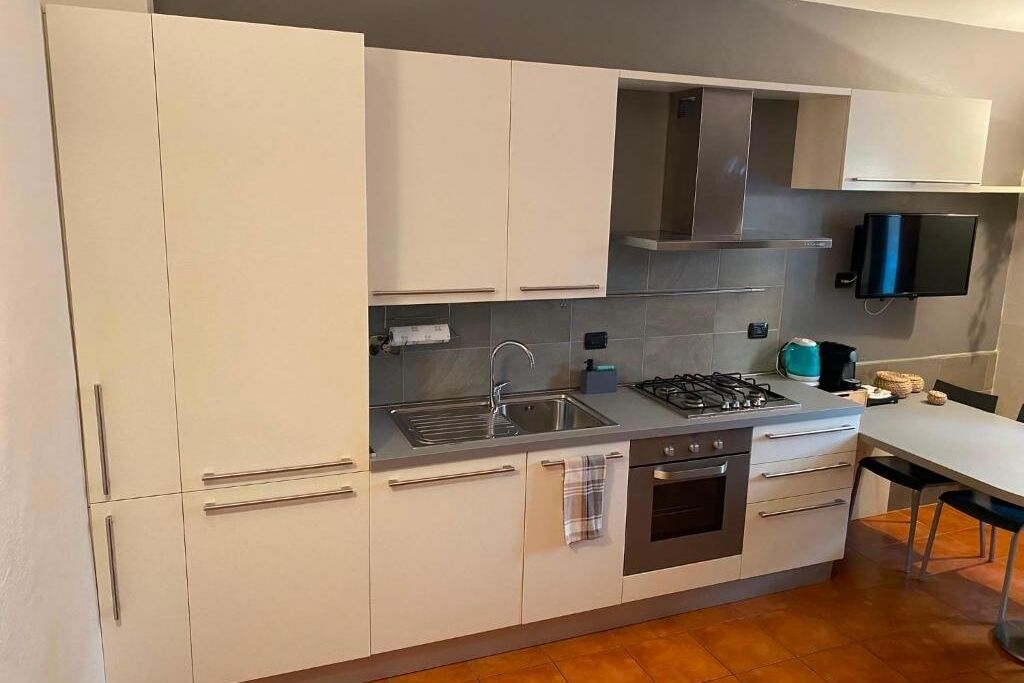 Eine moderne Küche mit weißen Schränken, einer Edelstahl-Spüle, einem Gasherd und einem eingebauten Backofen.