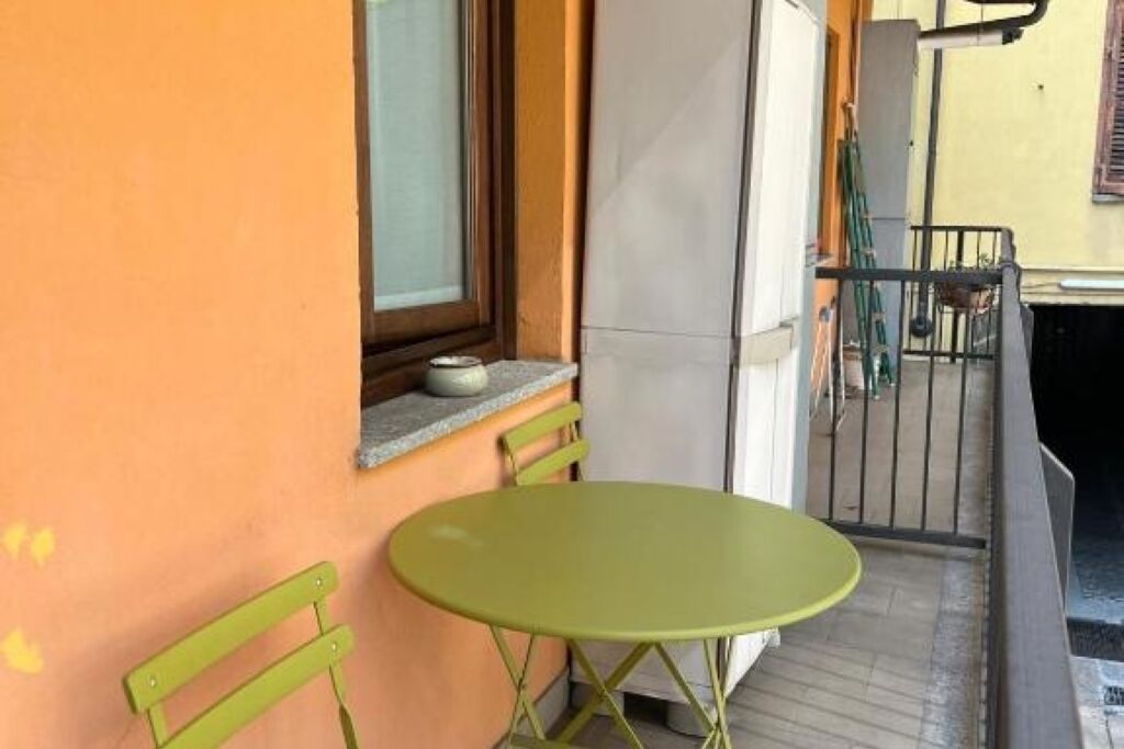 Ein kleiner Balkon mit einem grünen Metalltisch und -stühlen, einem Fenster und einem weißen Kühlschrank.