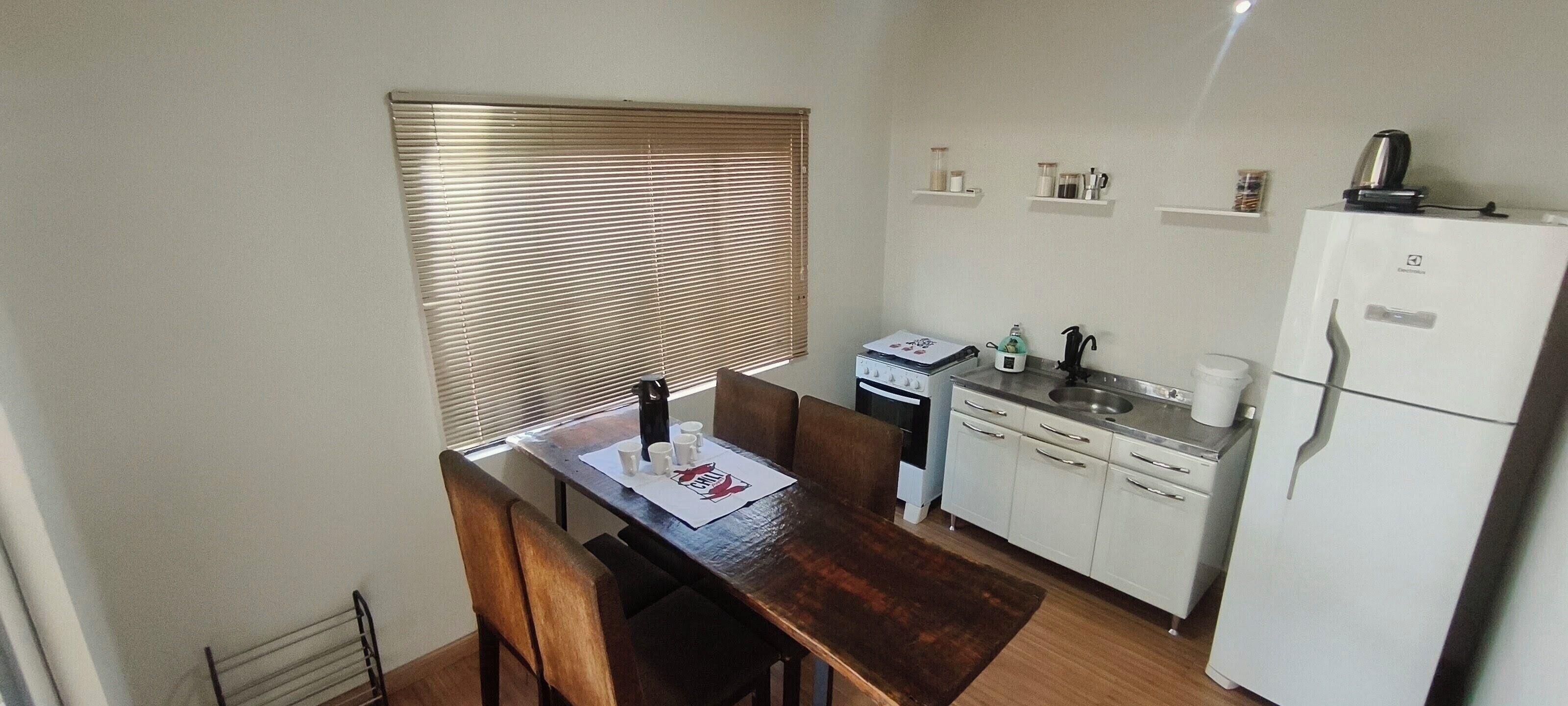 A compact kitchen with a dining table, a refrigerator, a stove, and a window with blinds.