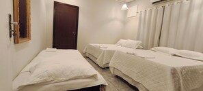 Habitación de hotel con dos camas individuales, una puerta, una ventana con cortinas y una lámpara colgante.