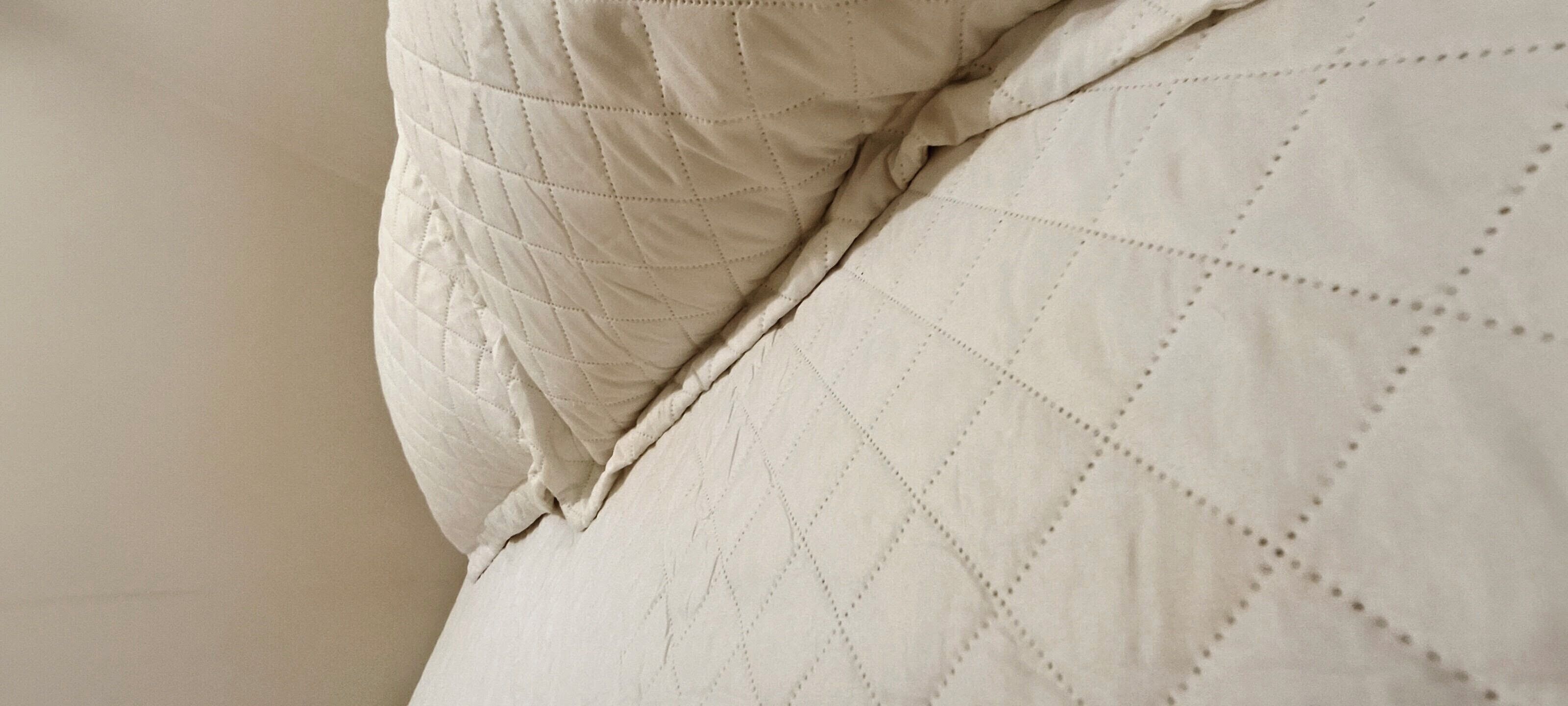 Een detail van een bed met een gewatteerd patroon en een kussen.