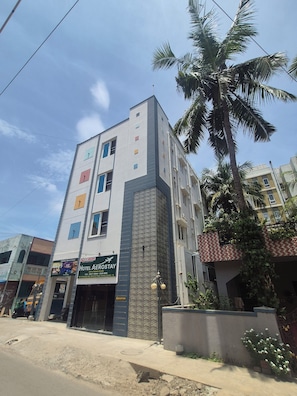 A multi-story hotel with a reception area, a visible staircase, and a palm tree in the foreground.