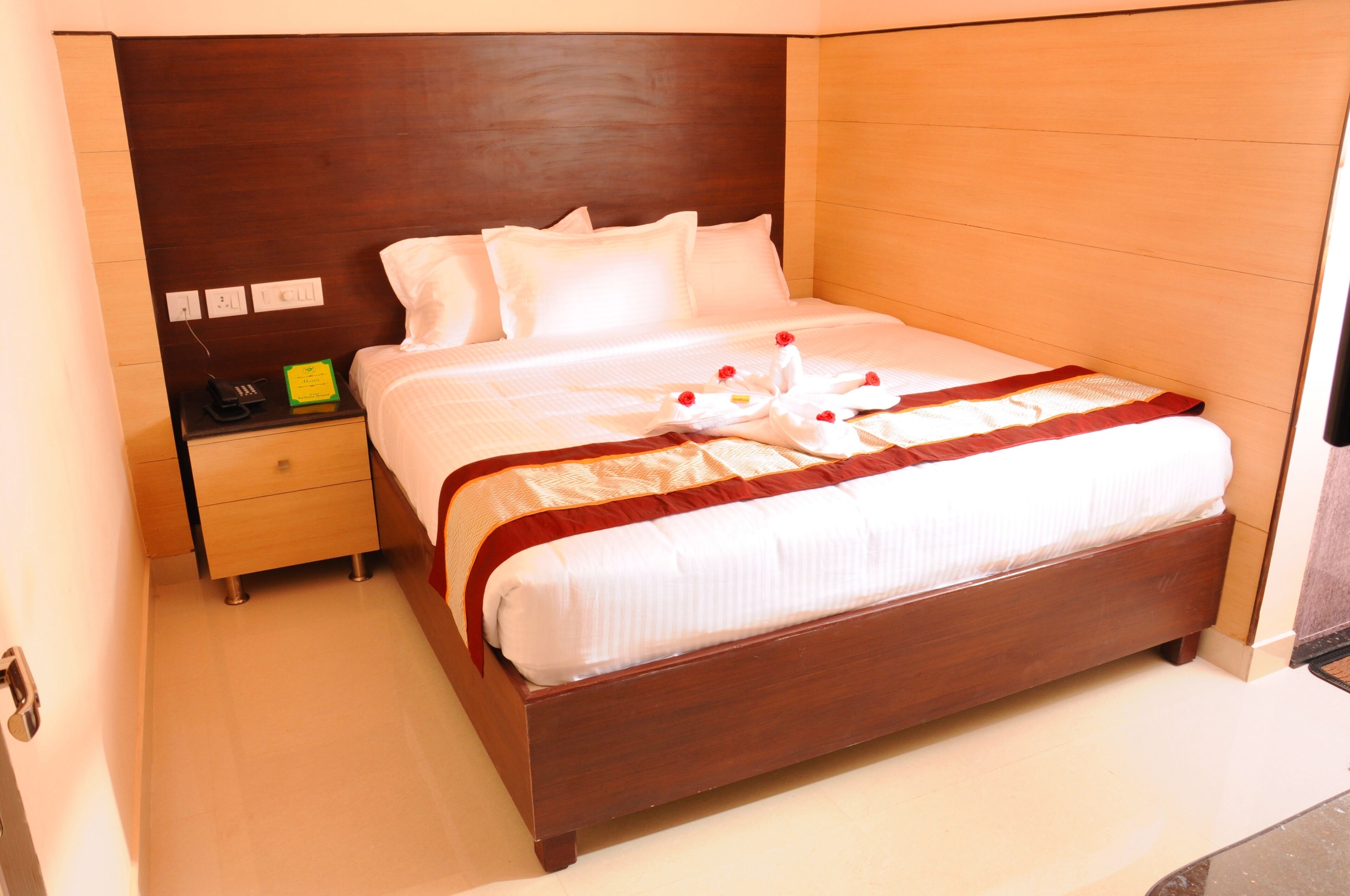 A hotel room with a wooden headboard, a bed with white bedding, a bedside table with a telephone, and a nightstand with a lamp.