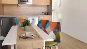 Cozinha compacta com micro-ondas, pequena geladeira e lava-louças. Há uma mesa de jantar com um banco e um vaso de planta sobre a mesa.