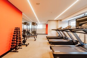 Un gimnasio con cintas de correr, máquinas de pesas y un estante con mancuernas.