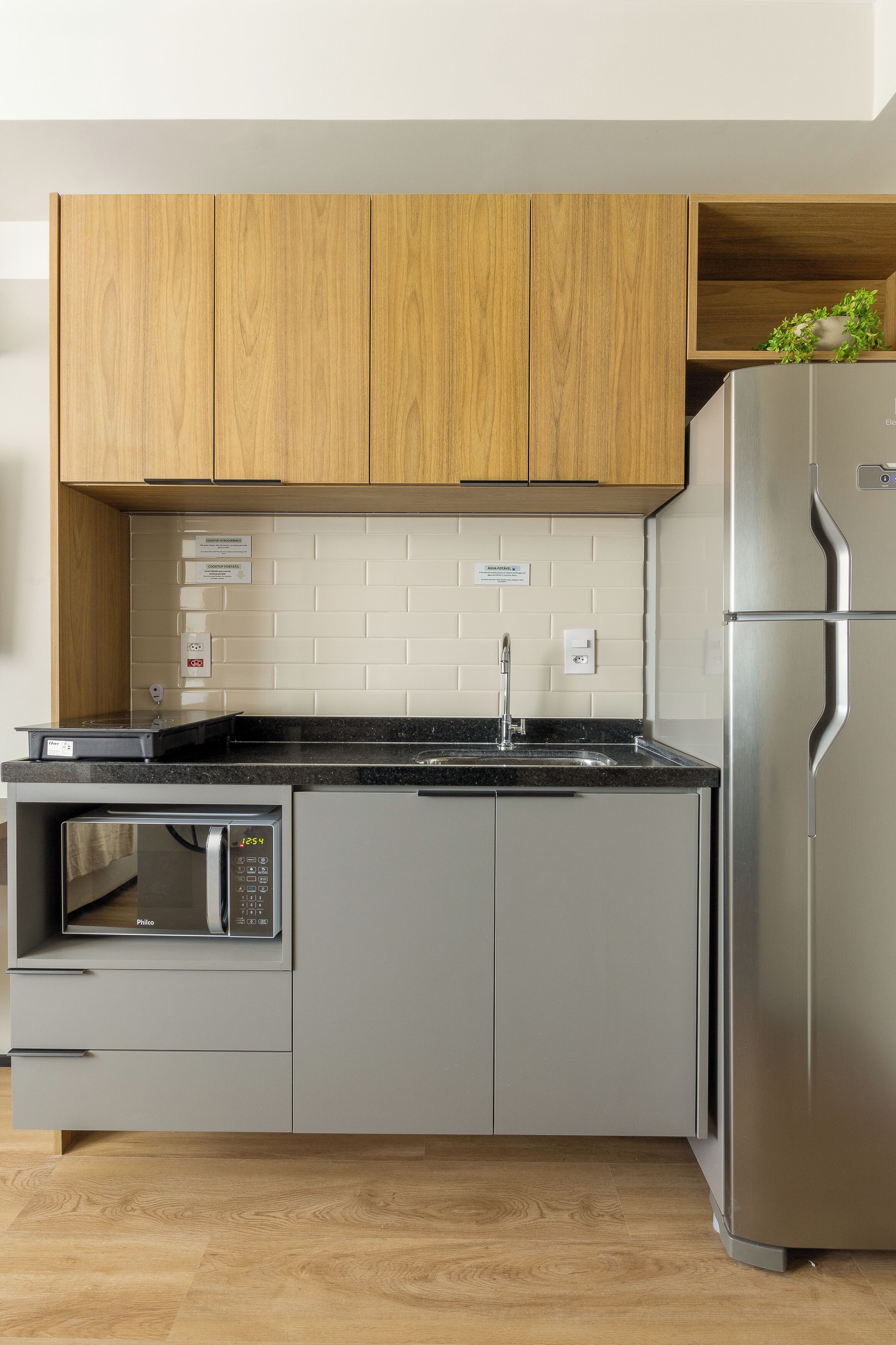 Una cocina moderna con armarios de madera, un refrigerador de acero inoxidable, un microondas integrado y una encimera negra.