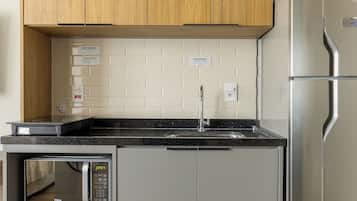 A modern kitchen with wooden cabinets, a stainless steel refrigerator, a built-in microwave, and a black countertop.
