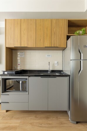 Una cocina moderna con armarios de madera, un refrigerador de acero inoxidable, un microondas integrado y una encimera negra.