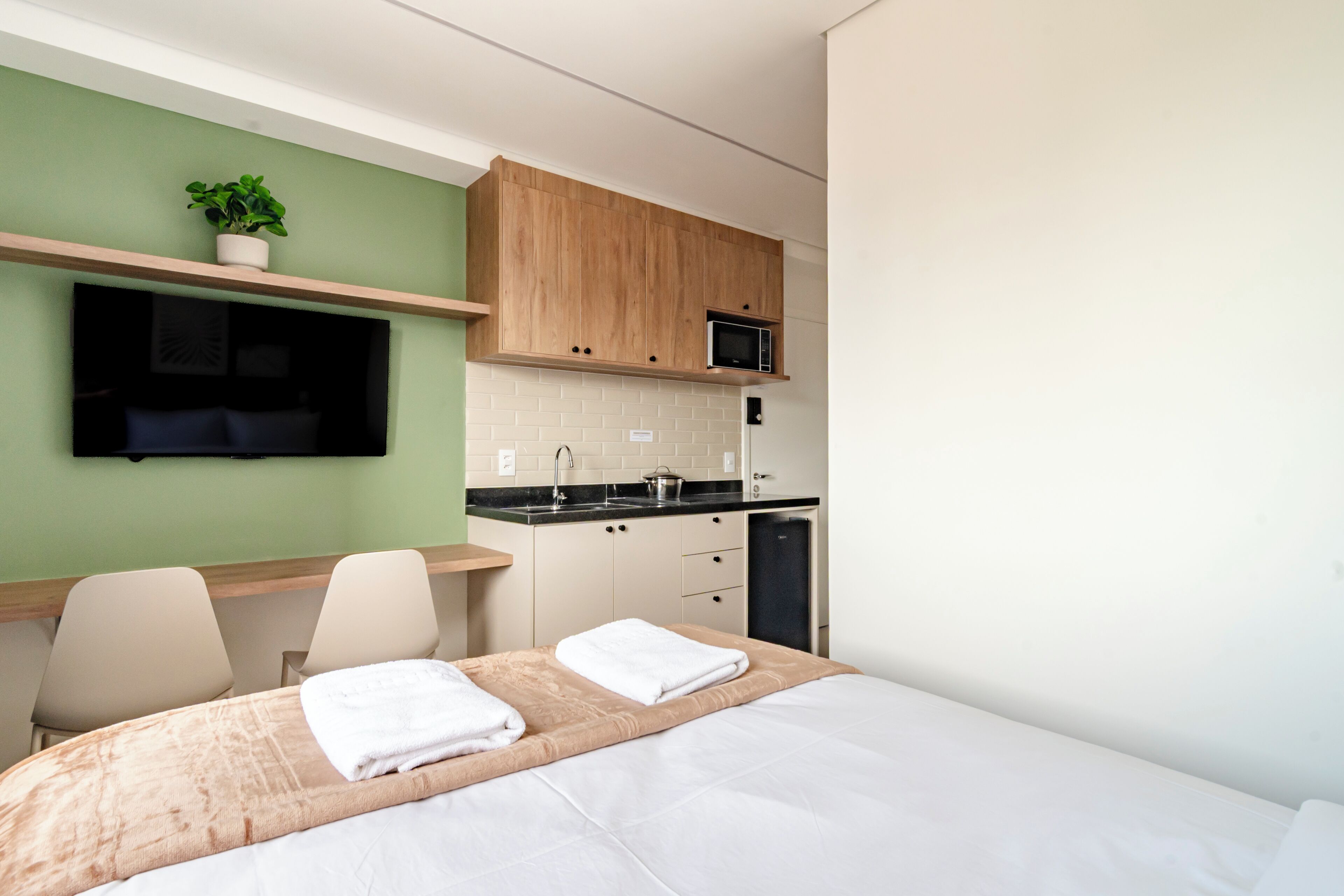 Una habitación de hotel moderna con una cama, un escritorio, una silla, un microondas y una pequeña cocina.
