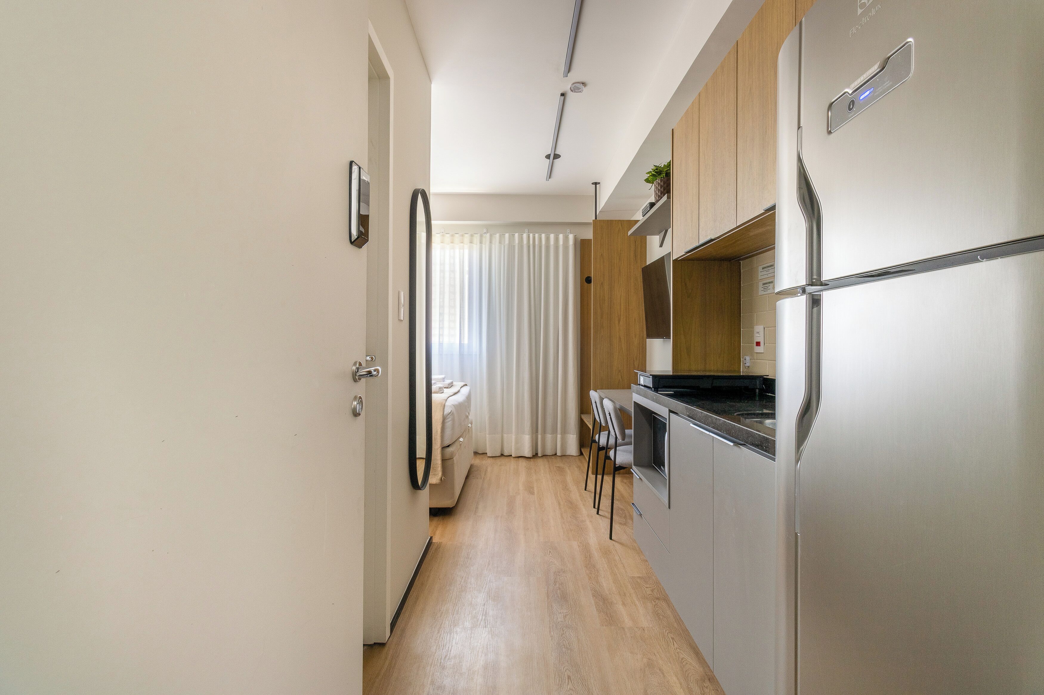 A narrow hallway leading to a bedroom with a bed and a bathroom with a shower curtain.