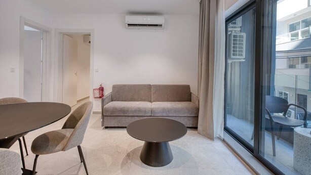 Una sala de estar moderna con un sofá, una mesa redonda de centro y una mesa de comedor con sillas.