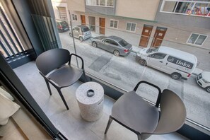 A balcony with two chairs and a small table, overlooking a street with parked cars and a delivery van. - Central 1BR Msida Suite | Balcony, Lift & Smart TV (L-Imsida)