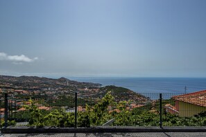 A coastal town with a view of the sea, a hilly landscape, and a fenced garden area. - Exclusive Oceanview 2-bedroom Apartment|Sol & Mar (Câmara De Lobos)