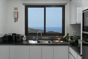 A kitchen with a large window, a Bosch coffee maker, a sink, and a view of the sea. - Exclusive Oceanview 2-bedroom Apartment|Sol & Mar (Câmara De Lobos)