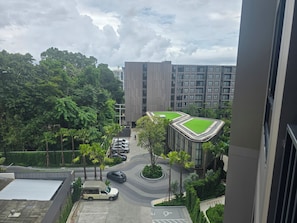 A residential area with modern buildings, a parking lot, and a green space with trees. - The Base • 1BR • Skyline View (Choeng Thale)