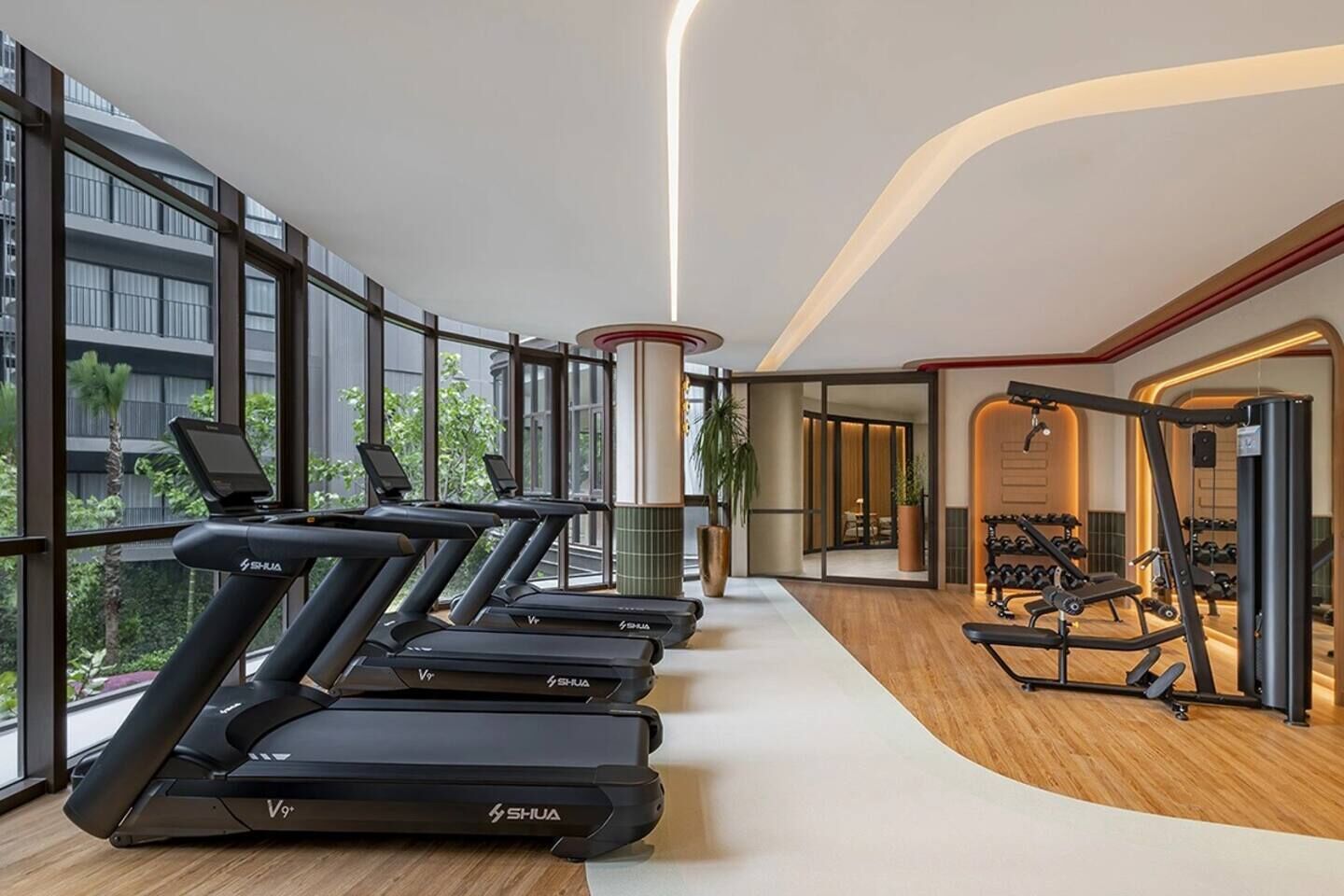 Ein modernes Fitnessstudio mit Laufbändern, Kraftgeräten und einem großen Fenster mit Blick auf ein Gebäude.