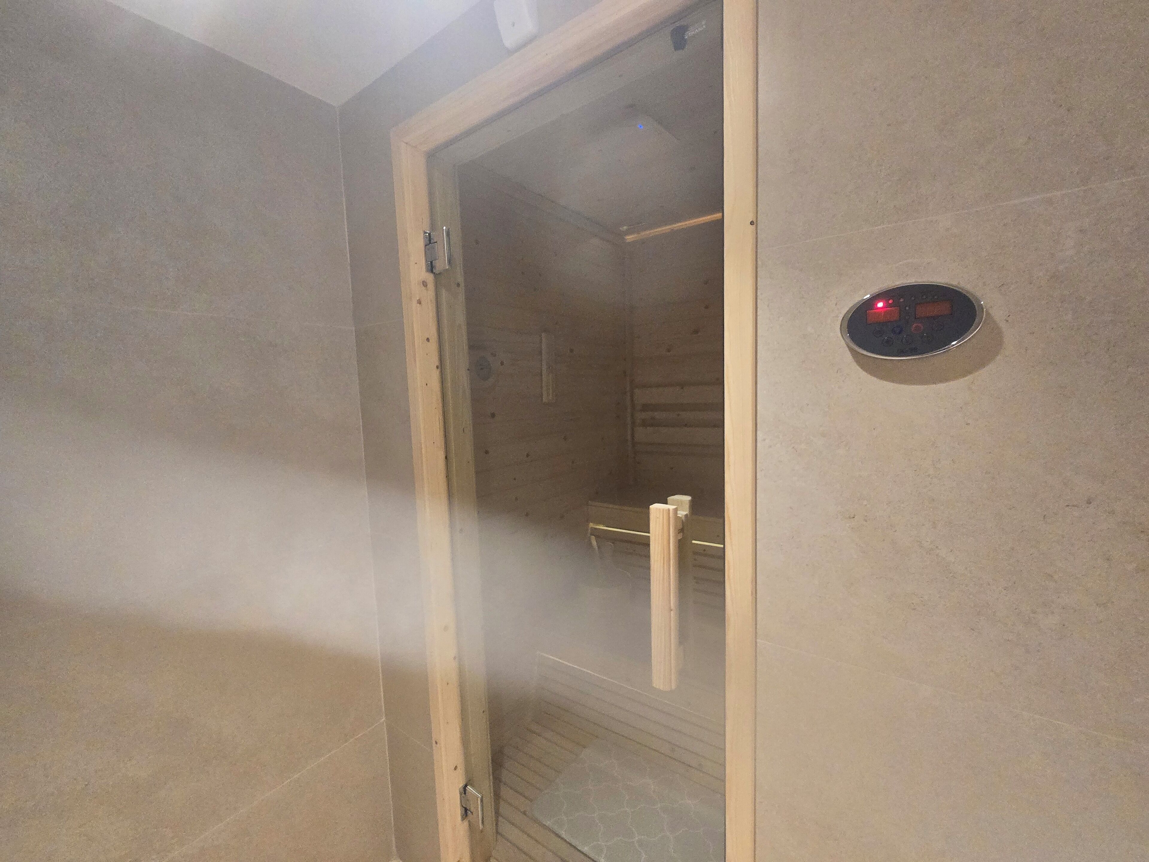 Una sauna con puerta de vidrio, un panel de control y un banco de madera en su interior.