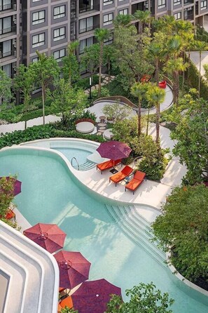 Ein Swimmingpool mit Liegestühlen und Sonnenschirmen, umgeben von Grünflächen und einem mehrstöckigen Gebäude.