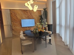 A modern dining area with a marble wall, a flat-screen TV, and a table with chairs. - The Base • 1BR • Skyline View (Choeng Thale)