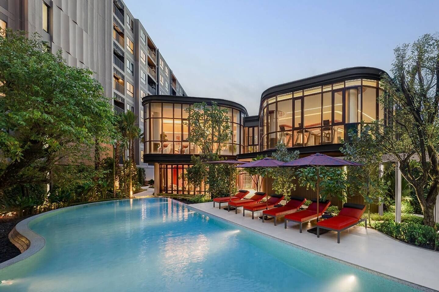 A modern hotel with a pool, lounge chairs, and a well-maintained garden.